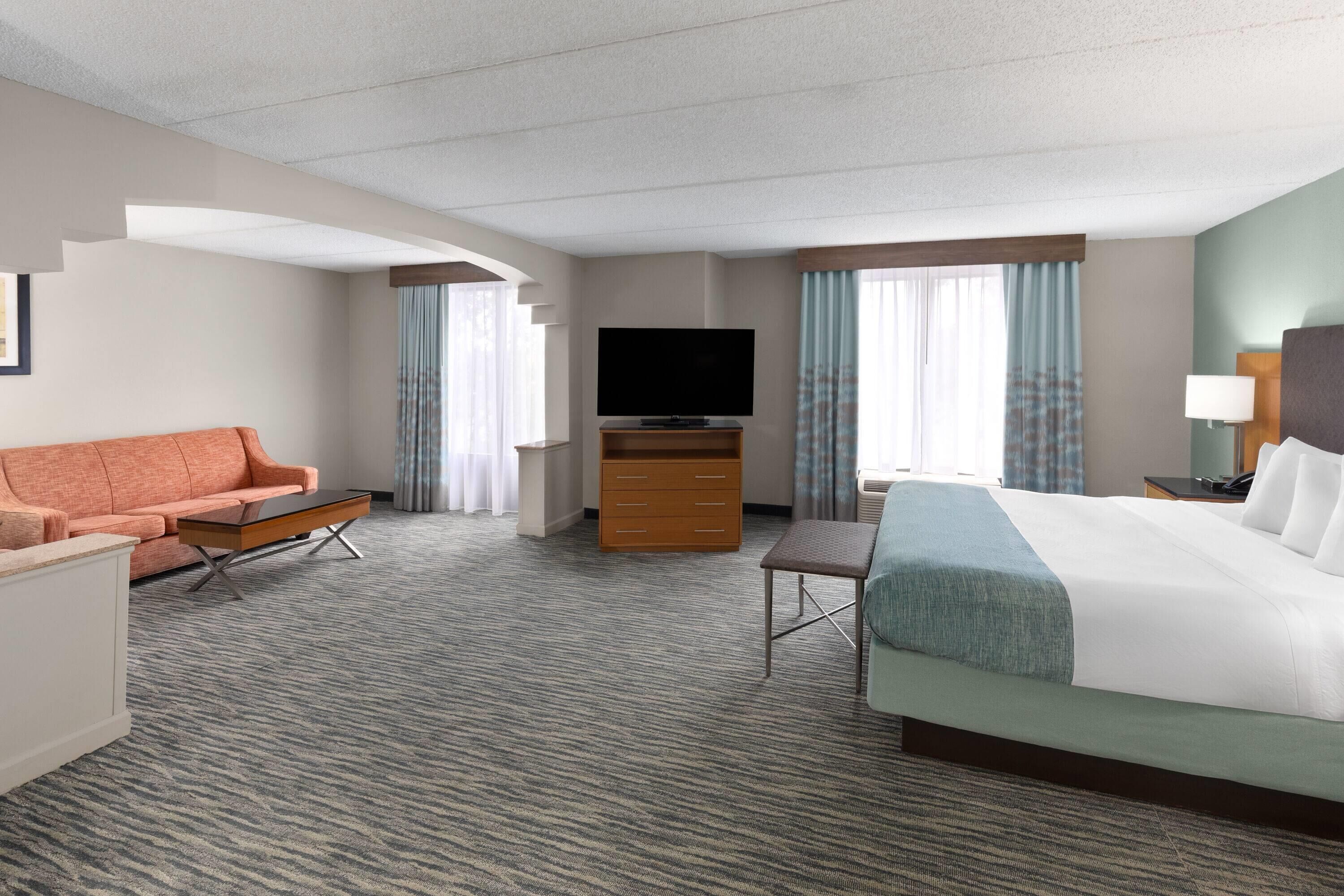 Ein Hotelzimmer mit einem großen Bett, einer Couch, einem Fernseher, einem Schreibtisch und einer Kommode.