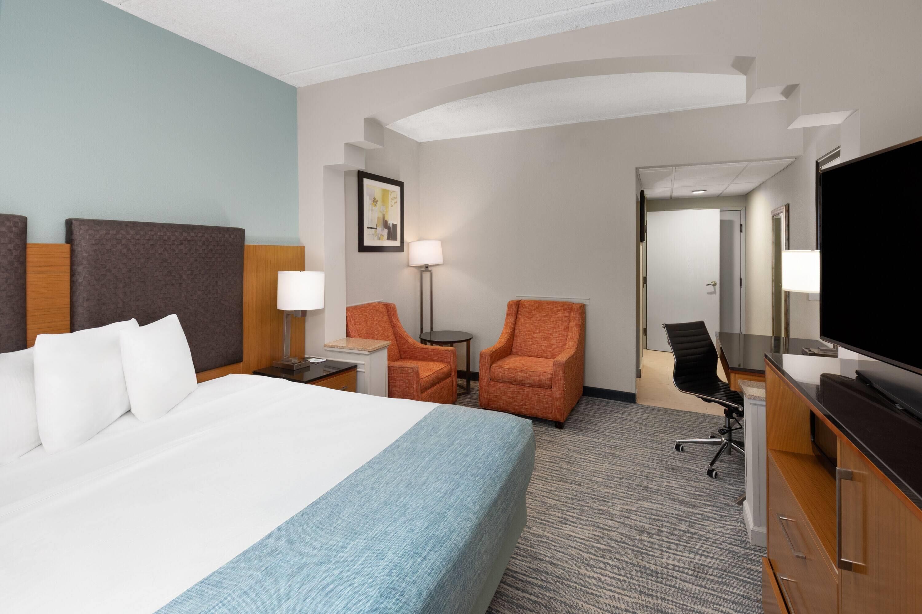 Une chambre d’hôtel avec un grand lit, deux fauteuils, un bureau, une télévision et un miroir.