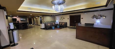 A spacious lobby with a reception desk, seating area, and a modern chandelier.