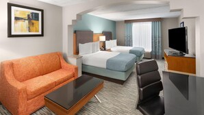 A hotel room with a bed, a sofa, a desk, a TV, and a painting on the wall. - Wingate by Wyndham Greensboro/Coliseum (Greensboro)