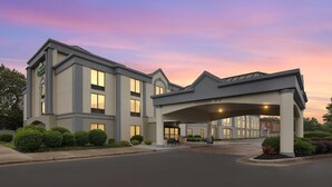 A hotel with a covered entrance, multiple windows, and a landscaped front yard. - Wingate by Wyndham Greensboro/Coliseum (Greensboro)