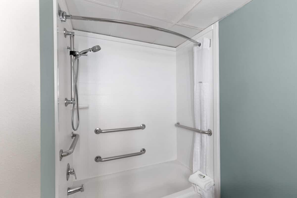 Une douche équipée de barres d’appui, d’un pommeau de douche à main et d’un porte-serviettes blanc.