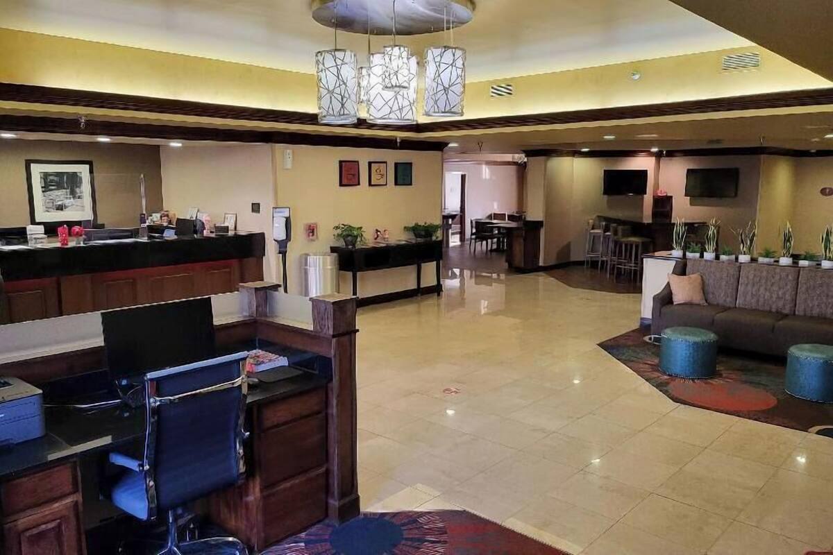 A hotel lobby with a reception desk, a dining area, and a seating area with a sofa and ottomans.
