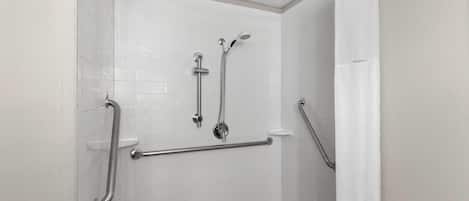 A shower area with white tiled walls, a grab bar, and a showerhead.