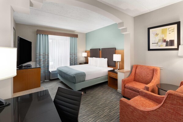 A hotel room with a bed, a desk with a telephone, a television, a chair, and a framed picture on the wall. - Wingate by Wyndham Greensboro/Coliseum (Greensboro)