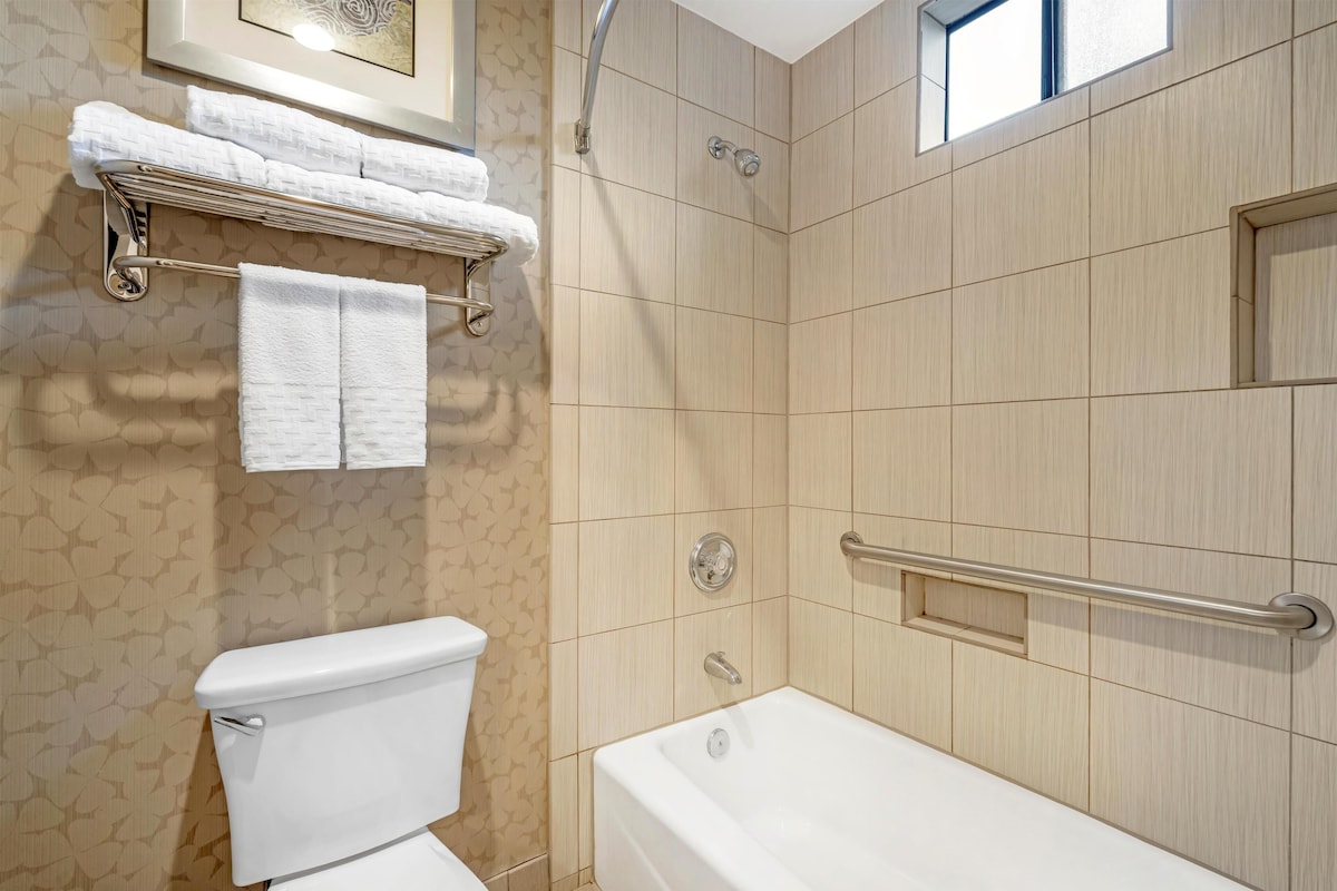 Ein modernes Badezimmer mit Toilette, Badewanne und Dusche. Handtuchhalter mit Handtüchern, ein Fenster und eine Tür sind vorhanden.