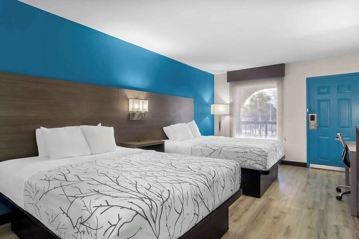 A hotel room with two beds, a blue door, and a view of the outside.
