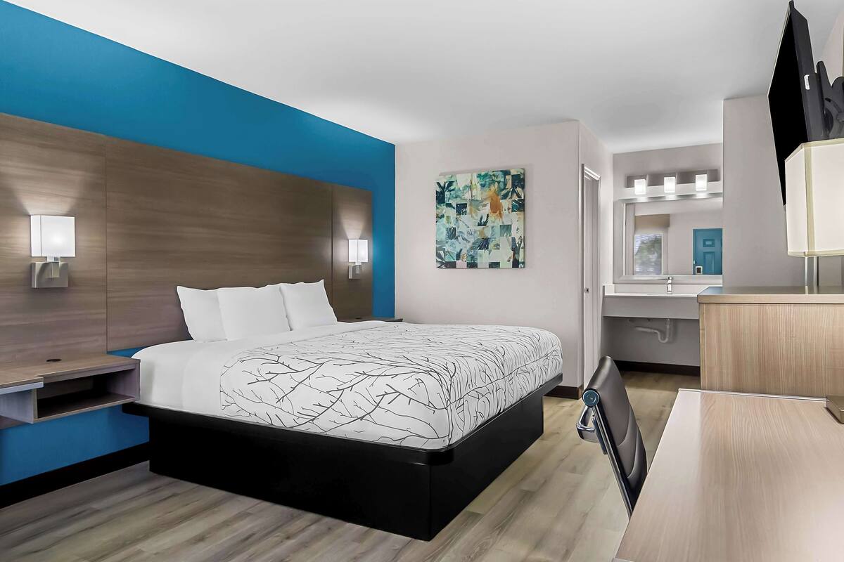 A modern hotel room with a large bed, bedside tables, a desk, and a mirror.