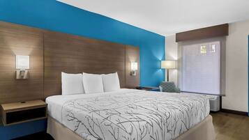 Habitación de hotel con una cama grande, dos mesitas de noche con lámparas, una ventana con persianas y una pared azul de acento.