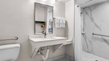 Un baño moderno con lavamanos, espejo y retrete blancos. Cuenta con una zona de ducha con puerta de cristal y paredes de mármol.