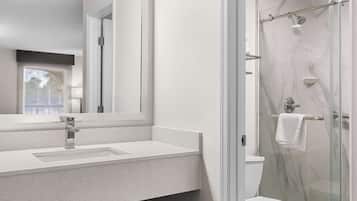 A modern bathroom with a glass-enclosed shower, a white sink, and a large mirror.