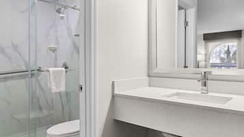 Een moderne badkamer met een douchecabine van glas, een wit toilet en een grote spiegel boven een wit aanrecht met wastafel.