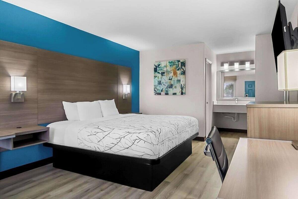 A modern hotel room with a bed, bedside tables, a desk, and a mirror.