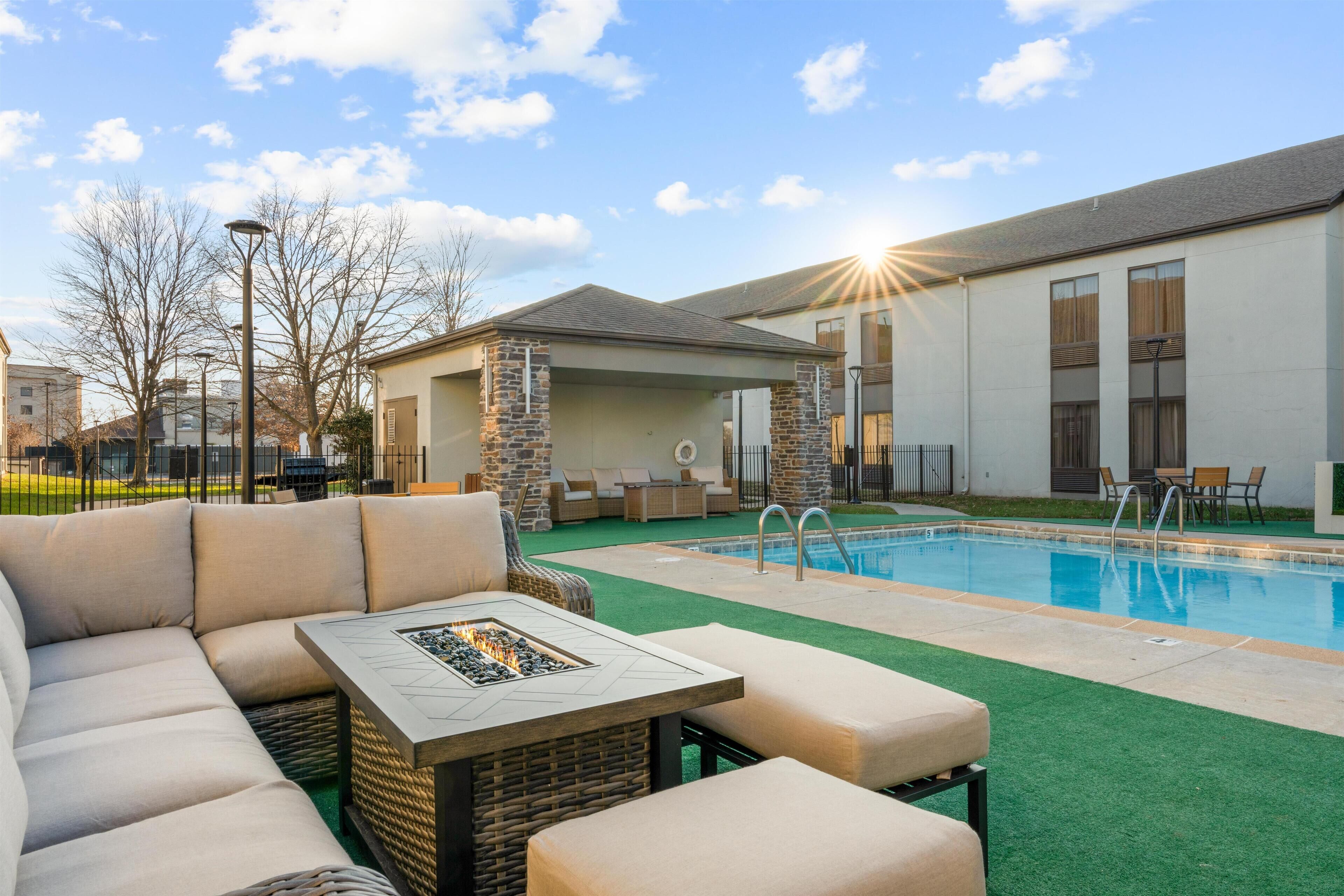 An outdoor pool area with a sofa, a fire pit, and a covered seating area.