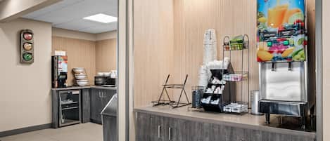 A hotel reception area with a juice dispenser, coffee machine, and a small refrigerator.