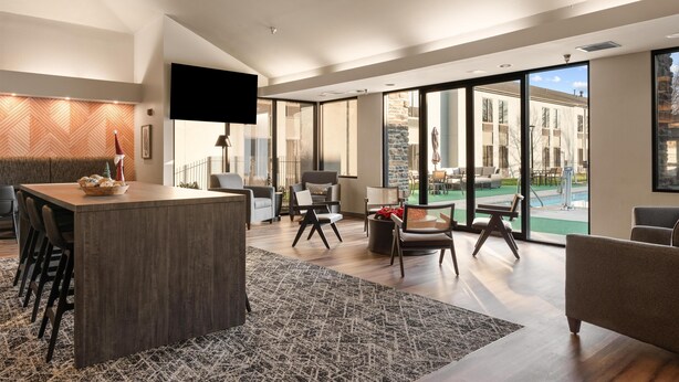 A spacious living area with a large island table, comfortable seating, and a view of an outdoor patio.