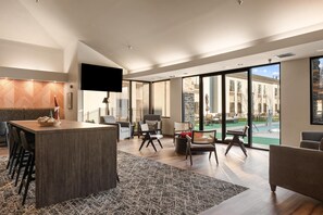 Uma sala de estar ampla com uma grande mesa central, assentos confortáveis e vista para um pátio externo.