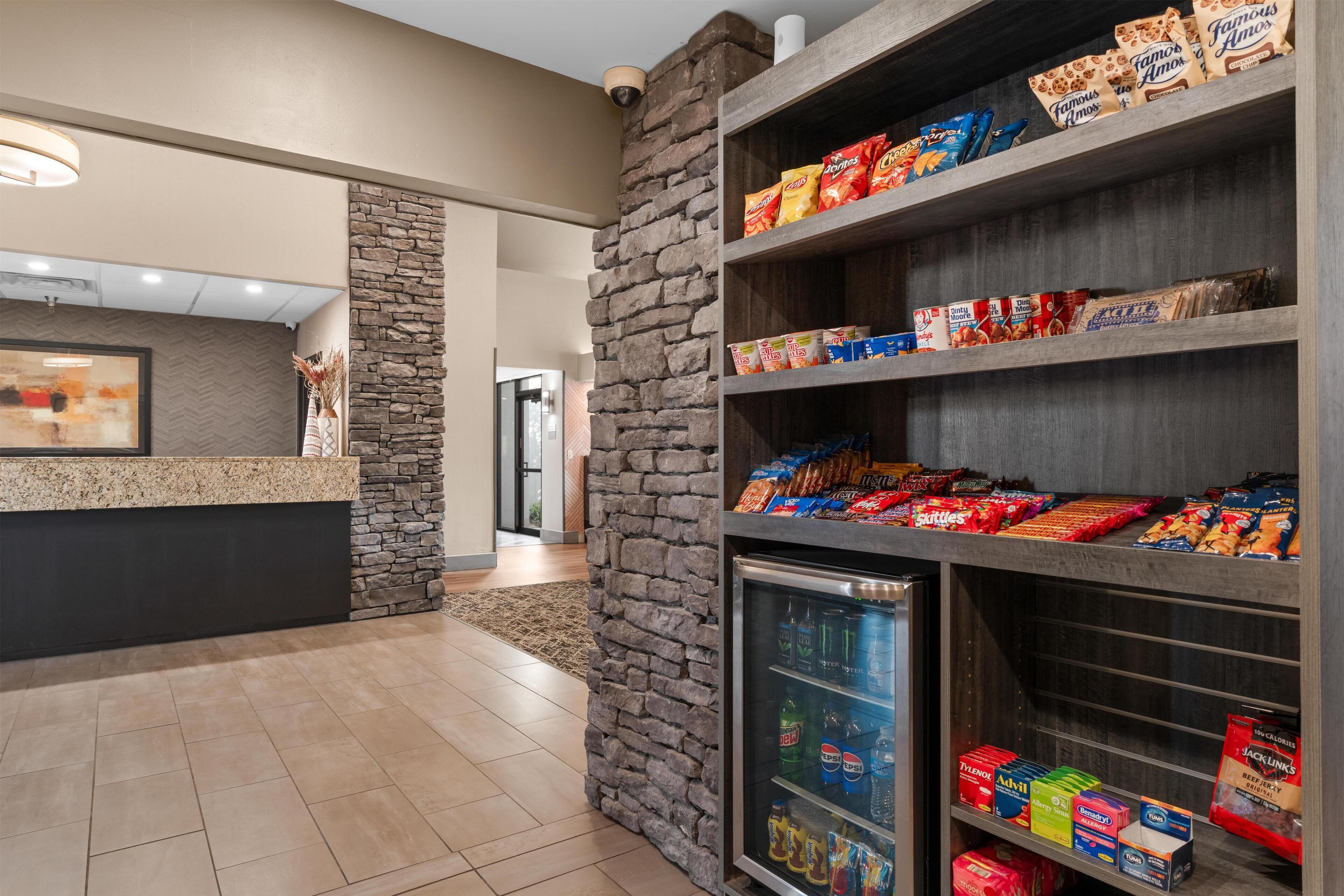A snack bar with a stone wall, a refrigerated display, and shelves stocked with various snacks and drinks.