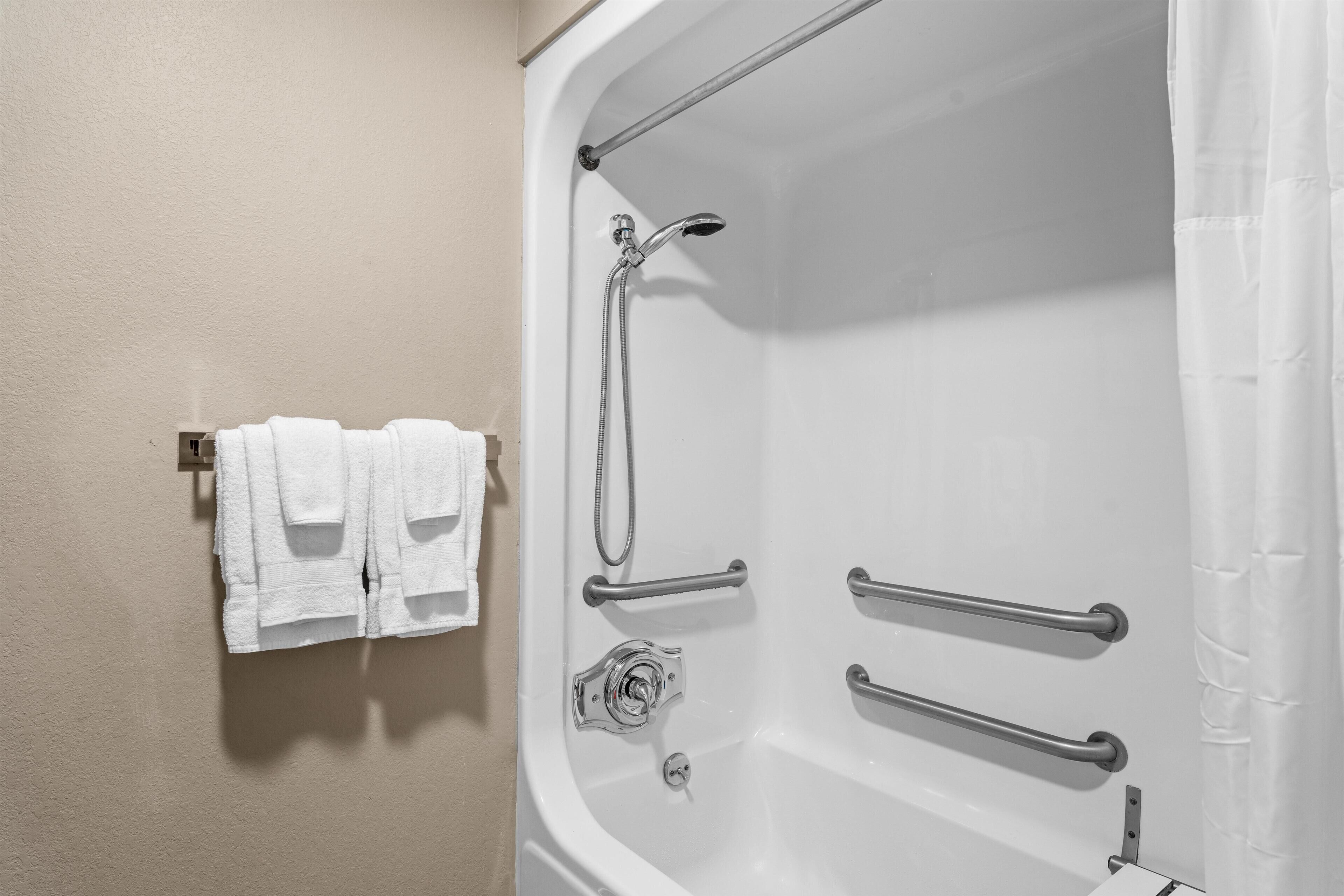 Un baño con bañera, barras de apoyo y un perchero con toallas.