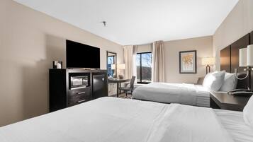 Habitación de hotel con dos camas, un escritorio con silla, televisión y ventana con cortinas.