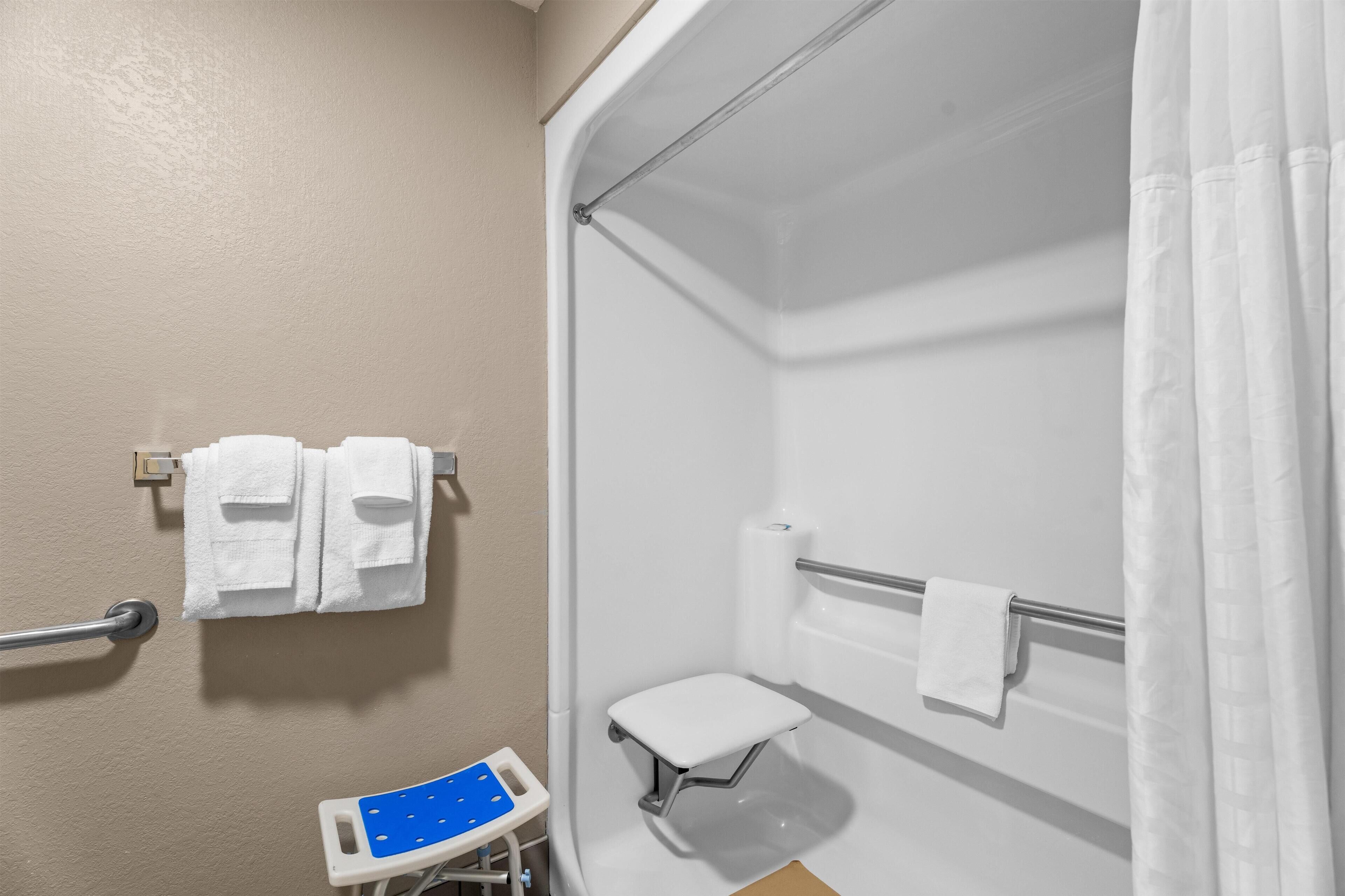 Une salle de bain avec une douche, un petit banc et une barre d’appui.
