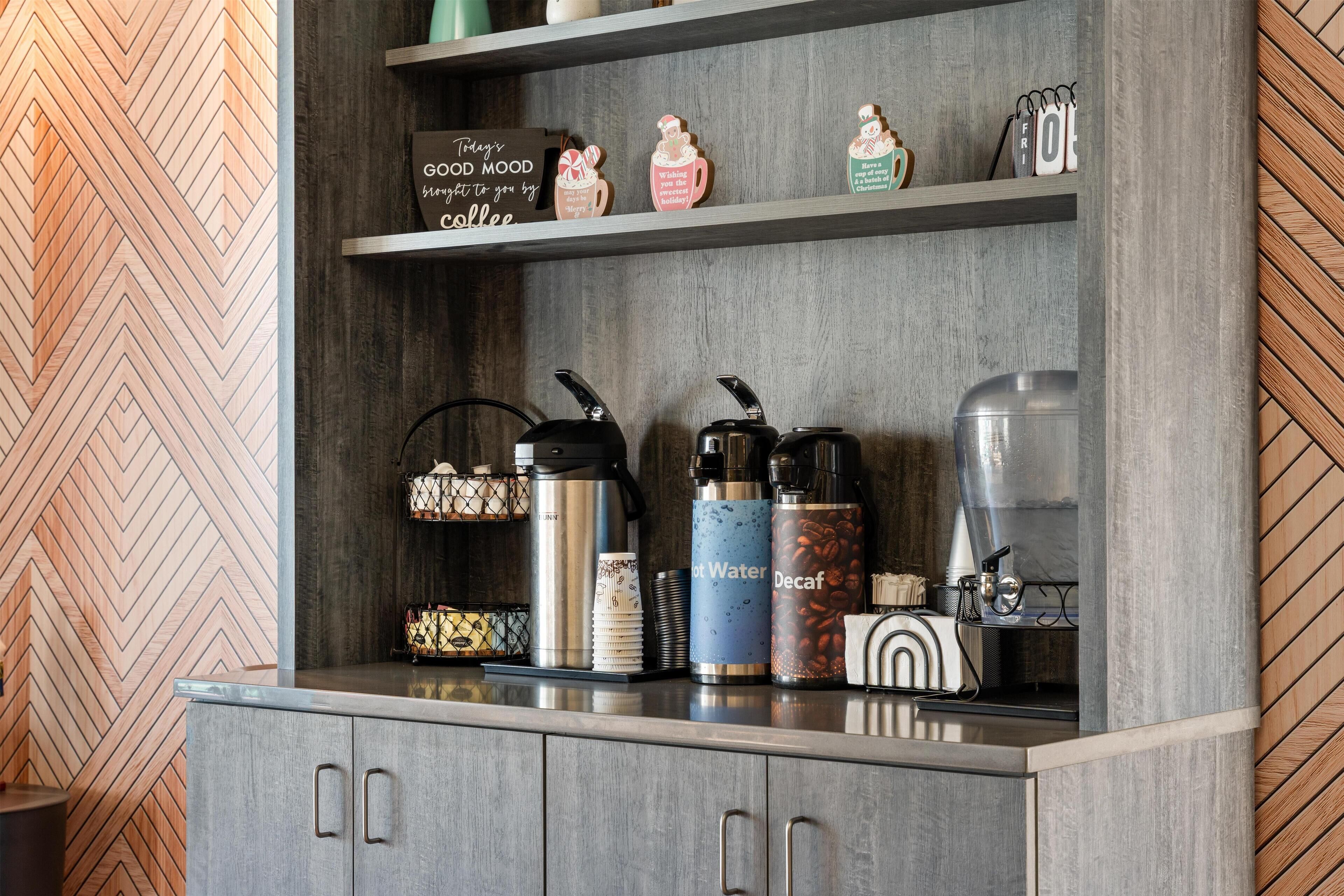 A kitchen area with a coffee station, including a coffee maker, water dispenser, and decaf coffee container.