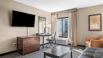 A hotel room with a flat-screen TV, a desk with a chair, a sofa, a dresser, and a large window with curtains.