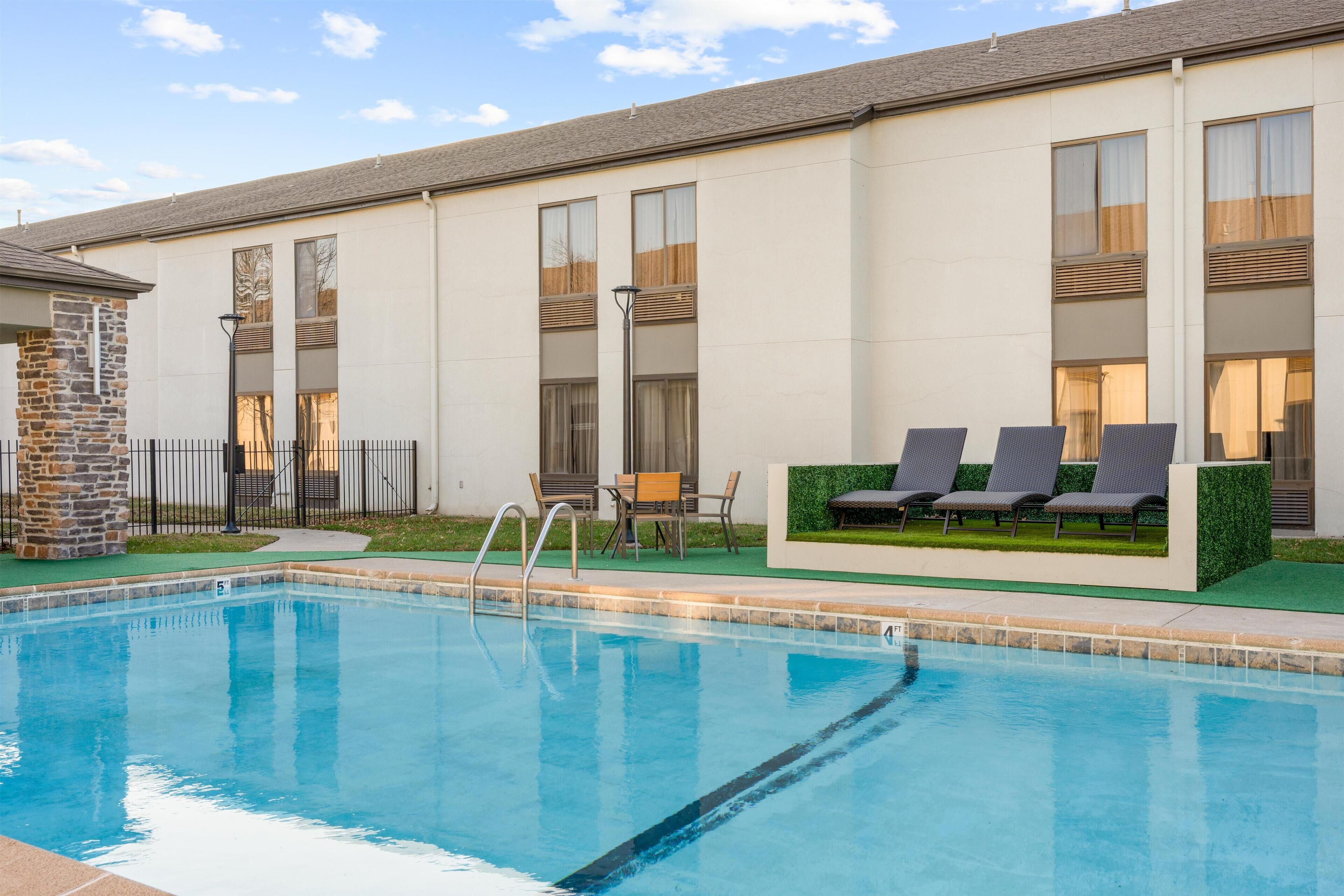 Un edificio moderno con piscina, mobiliario exterior y un pilar de piedra.