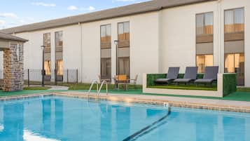 Un edificio moderno con piscina, mobiliario exterior y un pilar de piedra.