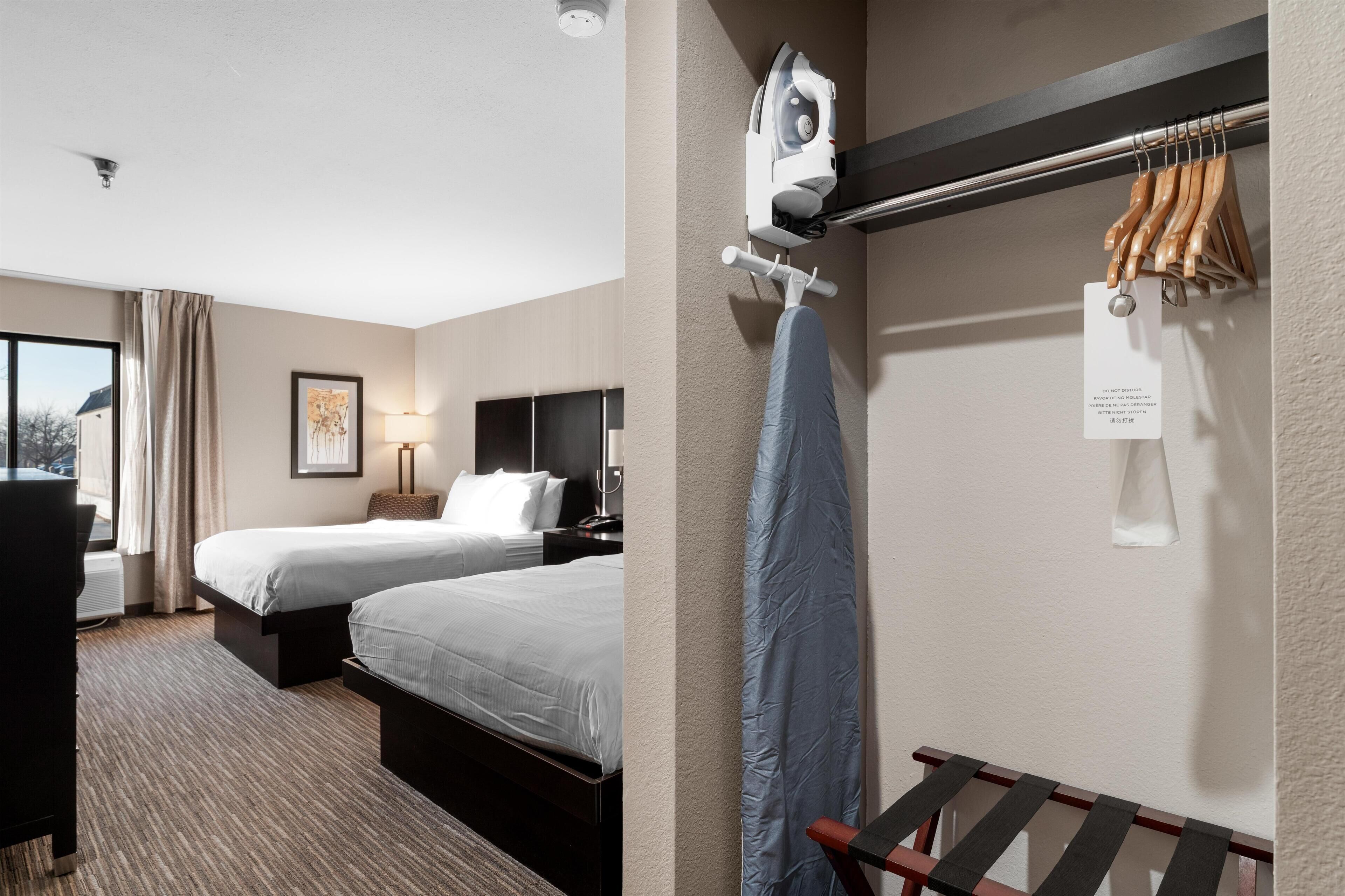 Habitación de hotel con dos camas, un escritorio, una silla, perchero y tabla de planchar fijada a la pared.