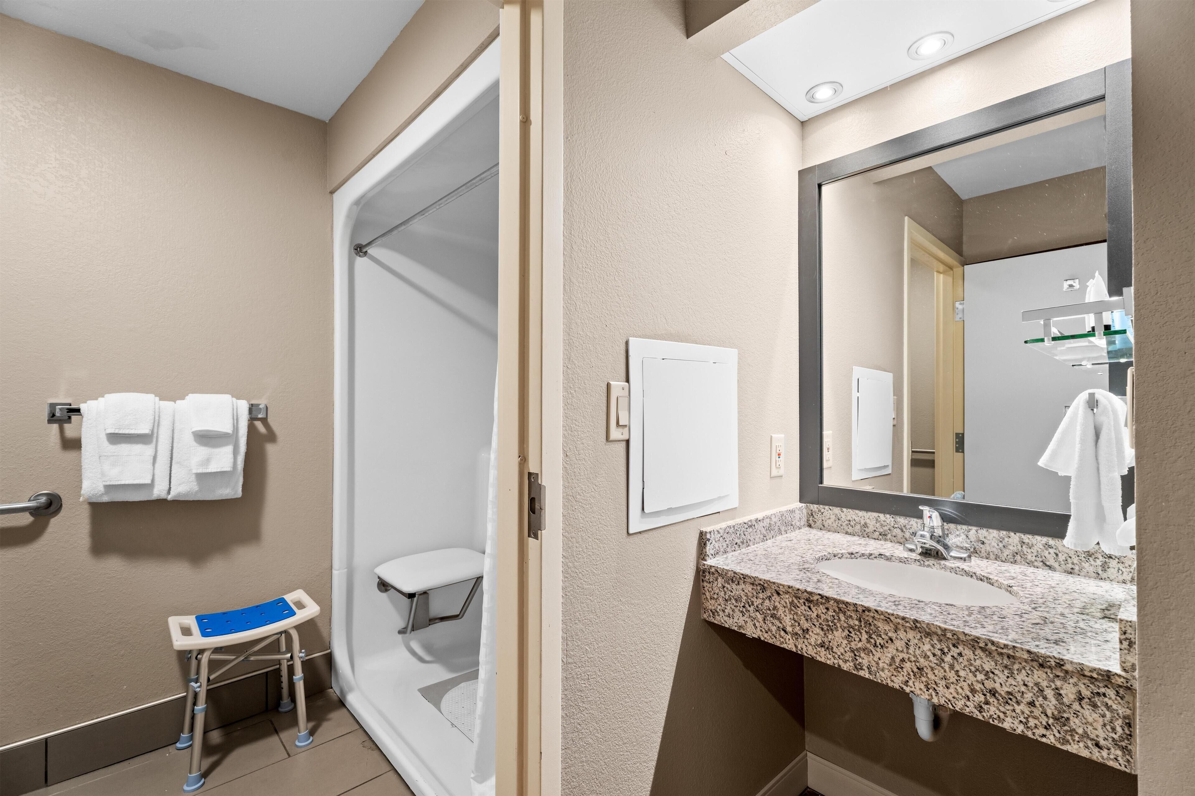 A bathroom with a shower, a sink with a granite countertop, and a mirror.