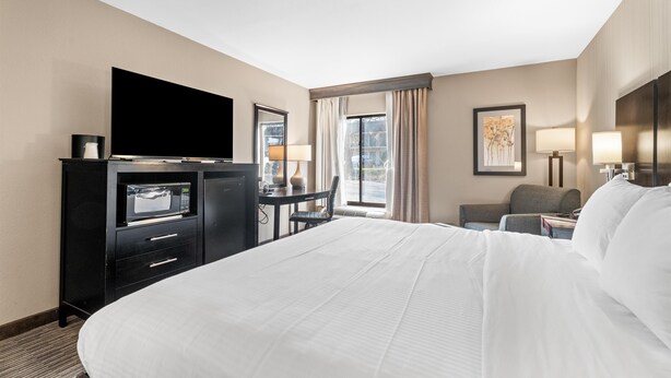 A hotel room with a large bed, a flat-screen TV, a desk with a lamp, a chair, and a window with curtains.
