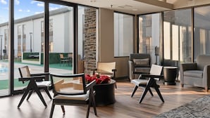 A spacious living area with large windows, modern furniture, and a view of a building and pool outside.