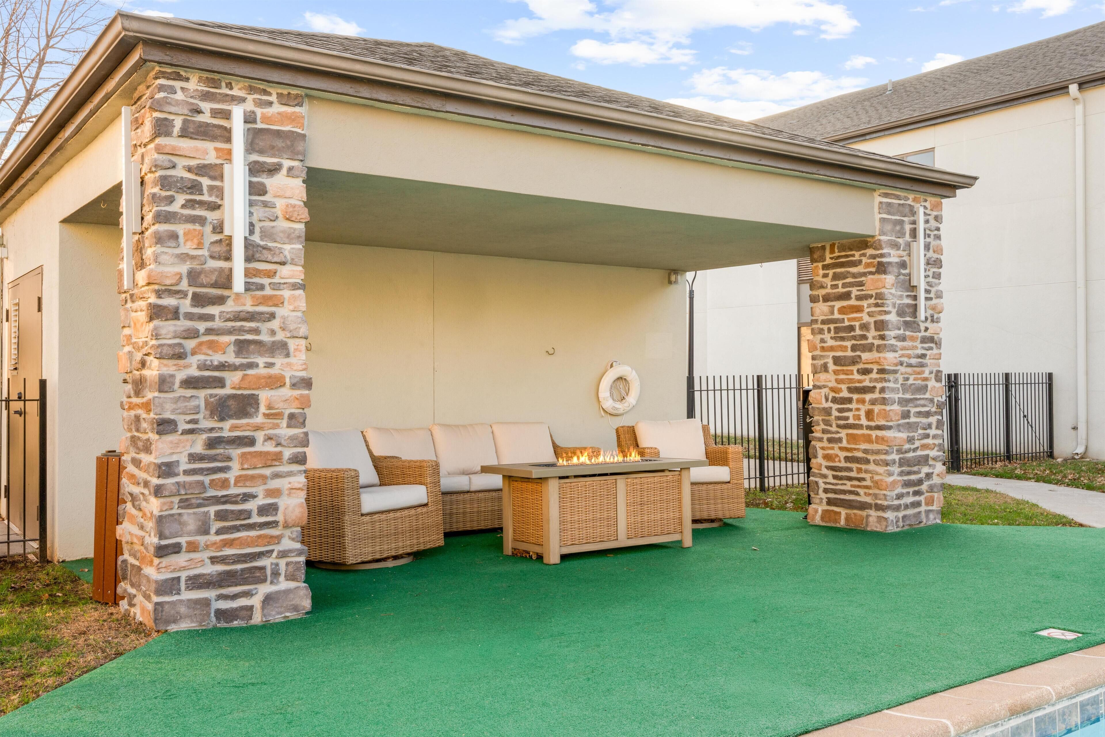Une terrasse extérieure agrémentée de piliers en pierre, de meubles en osier et d’un foyer.