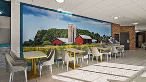 Un comedor con mesas y sillas, un mural con una escena campestre y una pared de ladrillo.