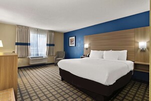 Habitación de hotel con una cama grande, un escritorio, una silla, una ventana con cortinas y un aire acondicionado de pared.