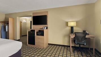 Habitación de hotel con cama, escritorio con silla, televisión, microondas y armario.