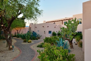 Stroll through a tranquil courtyard surrounded by lush greenery and desert plants, featuring a shaded area beneath a wooden pergola.