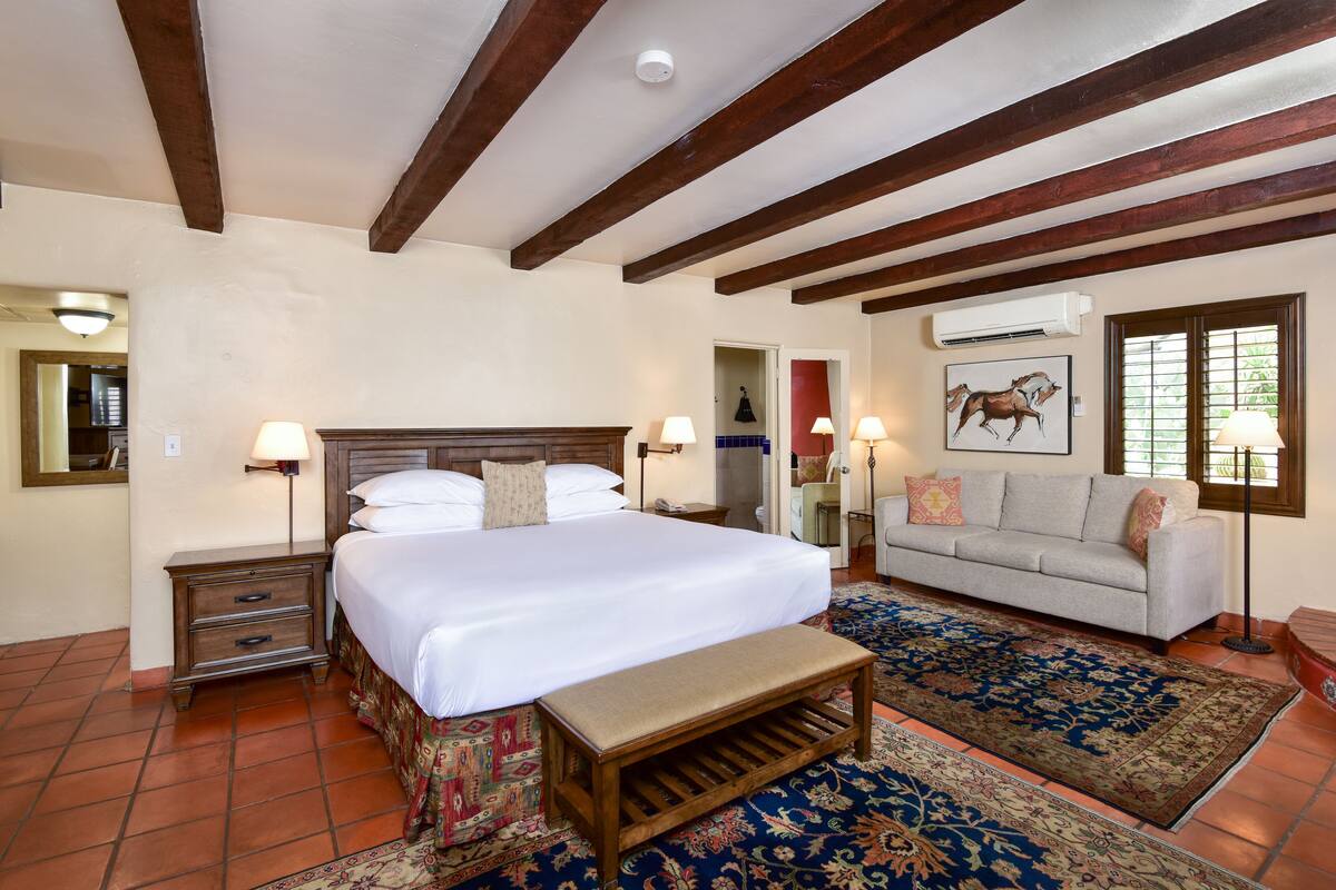 Une chambre à coucher avec un grand lit, un banc, un canapé et un tapis à motifs.
