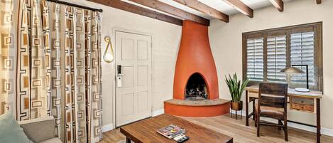 A living room with a fireplace, a sofa, a coffee table, and a desk with a chair.