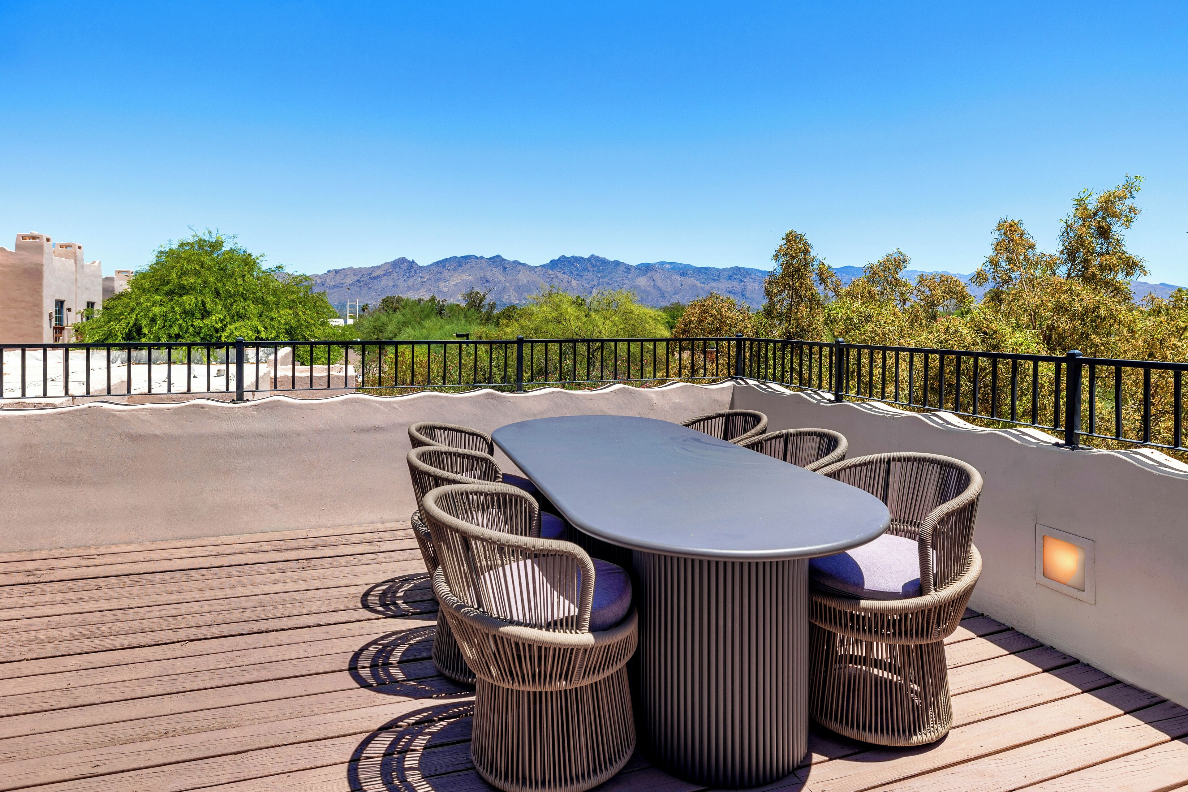A rooftop patio with a table and chairs, a view of mountains, and a clear sky.