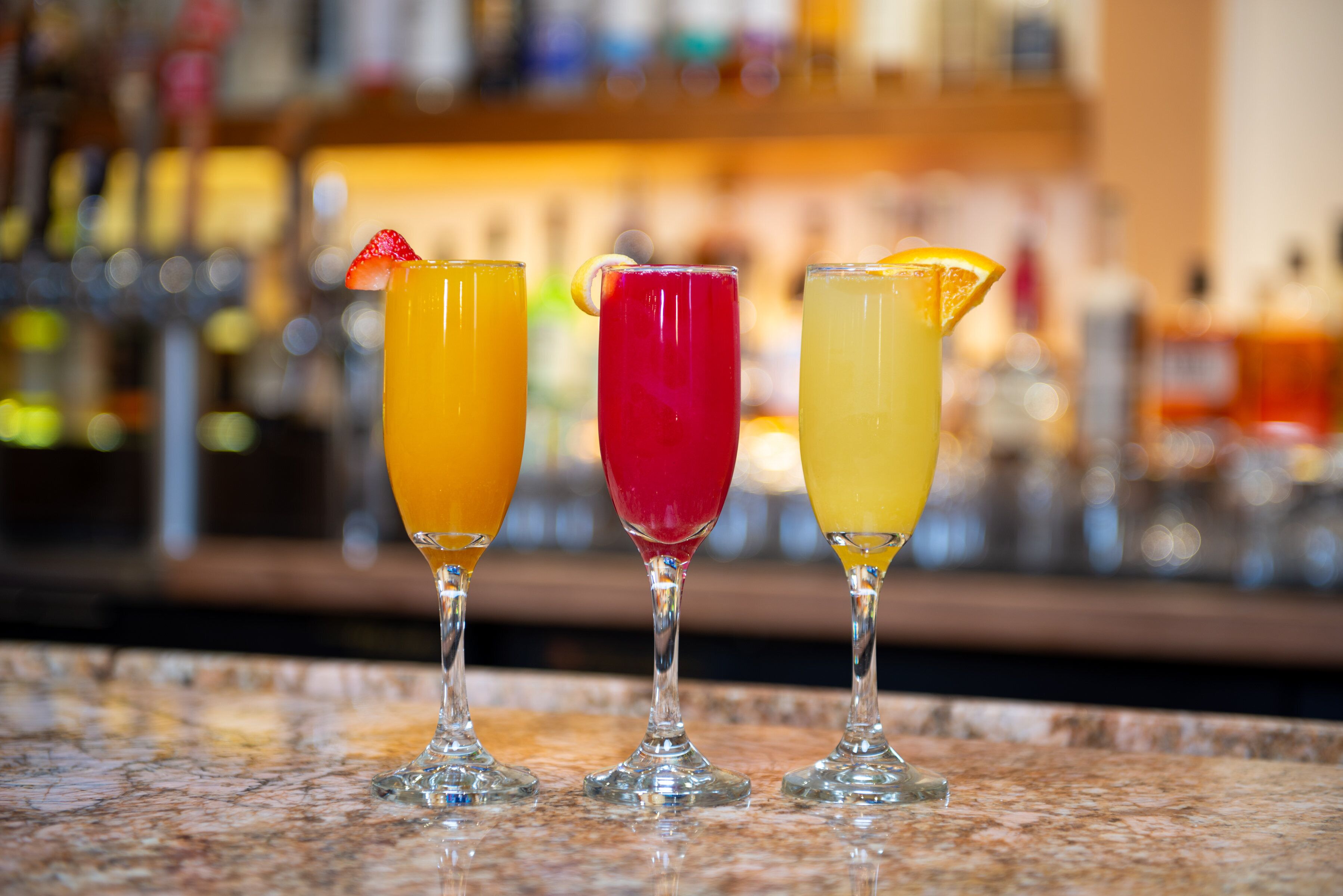 Drie cocktails op een barkruk, met op de achtergrond vage flessen.