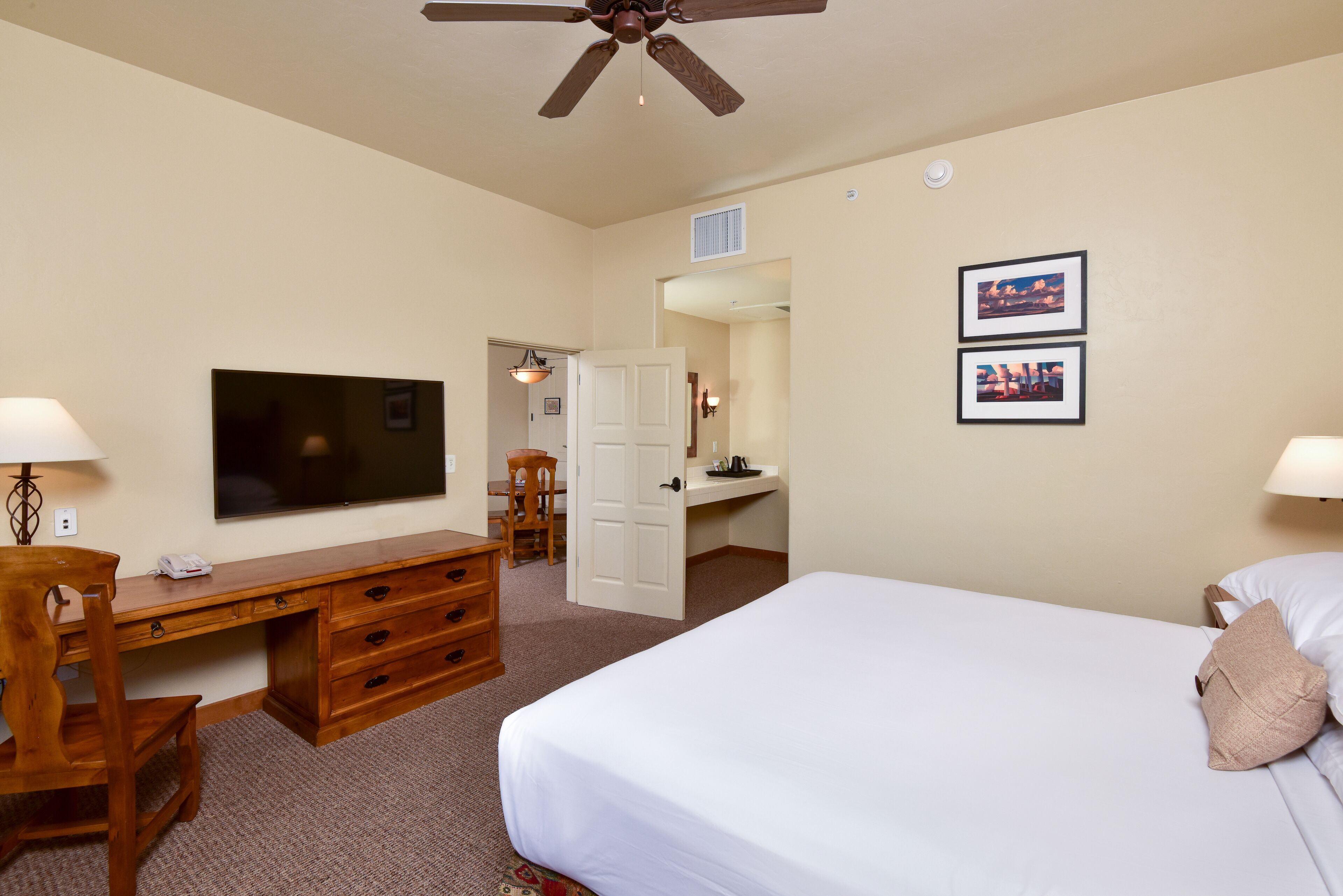 A hotel room with a bed, desk, chair, television, and two framed pictures on the wall.