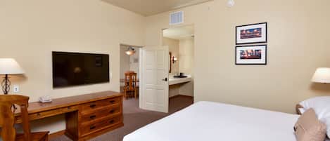 A hotel room with a bed, desk, chair, television, and two framed pictures on the wall.