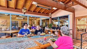 Un restaurante con mesas y sillas de madera, ventanas amplias y suelo de baldosas.
