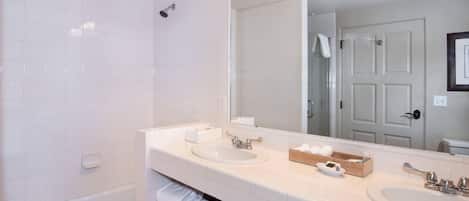 A modern bathroom with two sinks, a large mirror, and a shower.