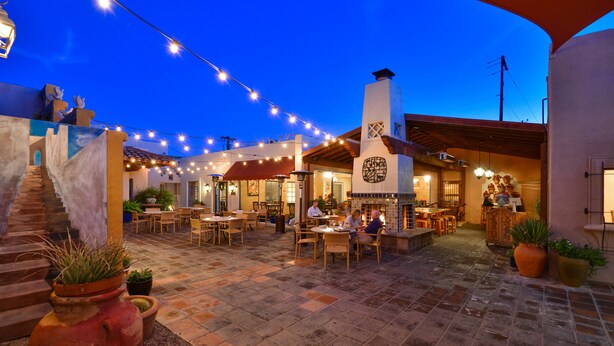 Un patio al aire libre con mesas, sillas, luces colgantes y plantas en macetas.