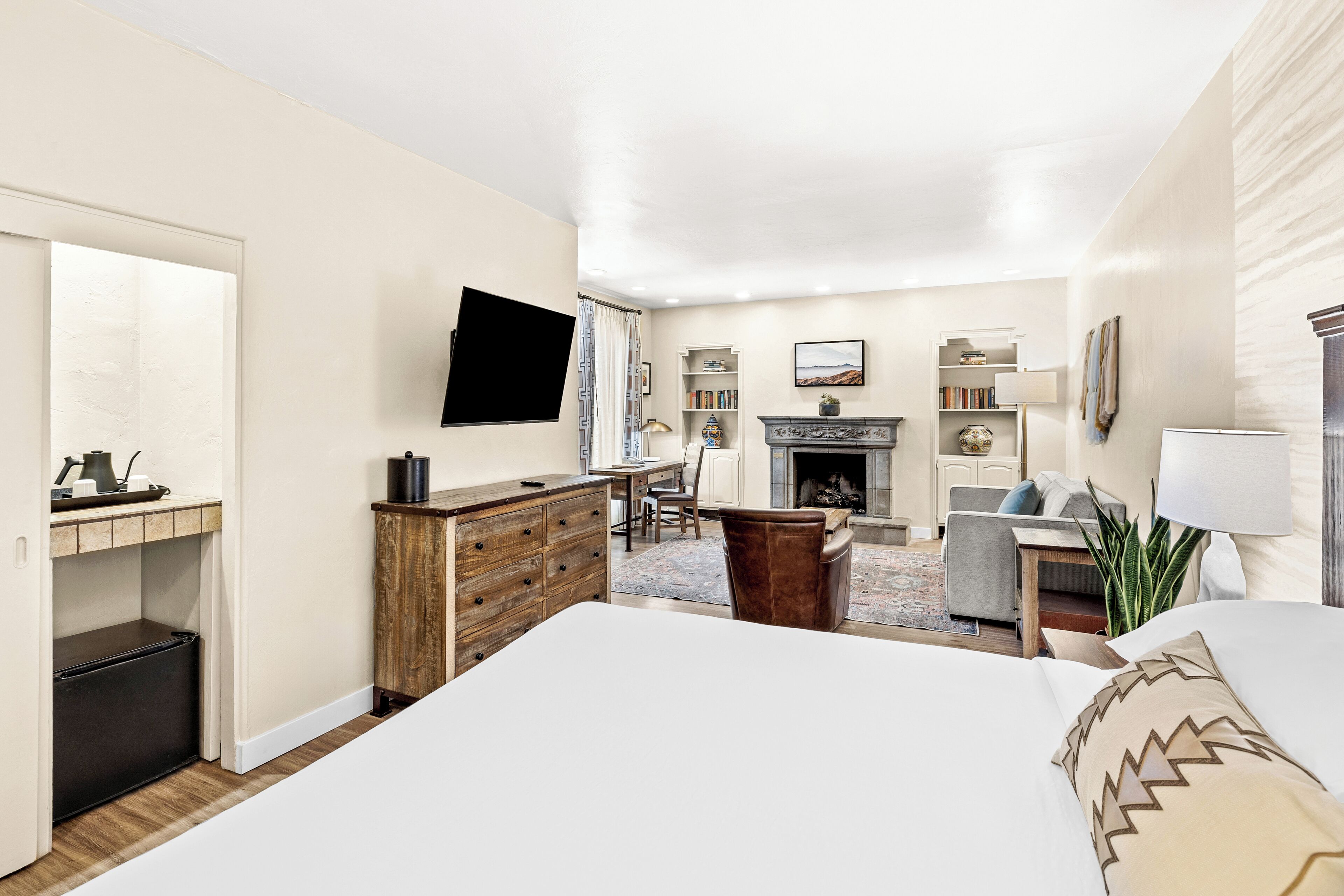 A hotel room with a bed, a desk, a chair, a fireplace, and a television.