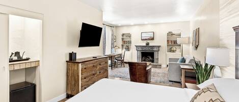 A hotel room with a bed, a desk, a chair, a fireplace, and a television.