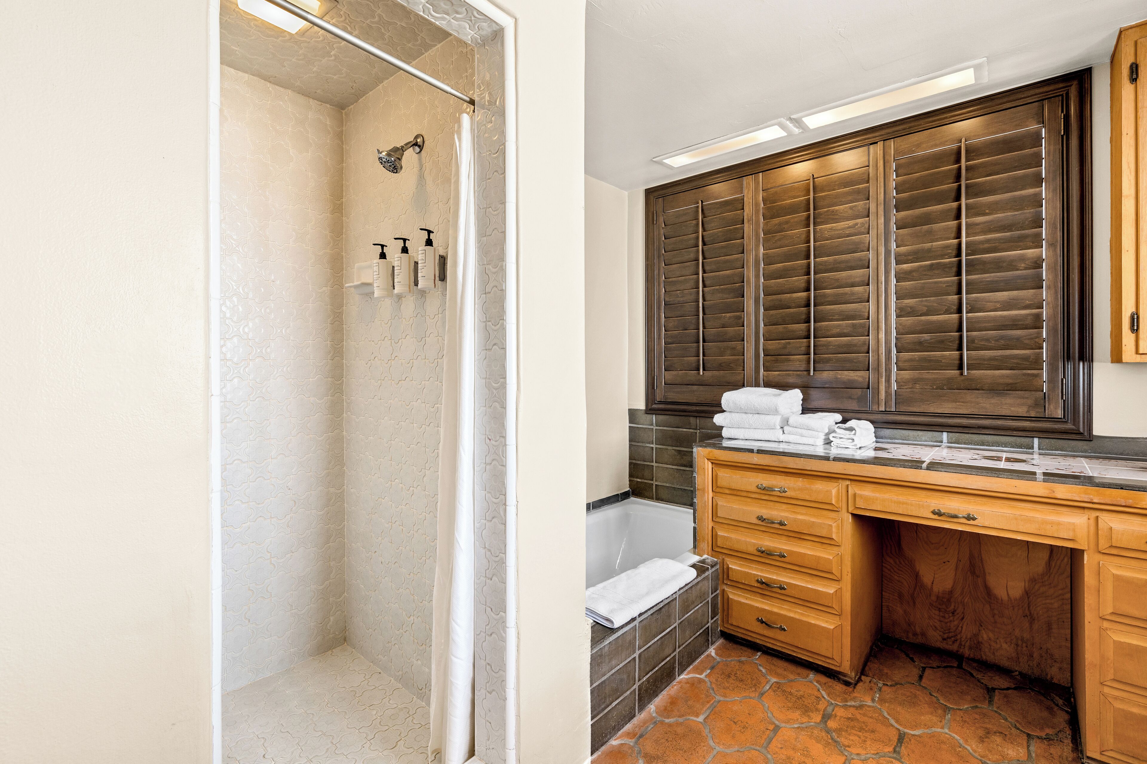 A bathroom with a shower, a bathtub, and a vanity with a large mirror and wooden cabinets.